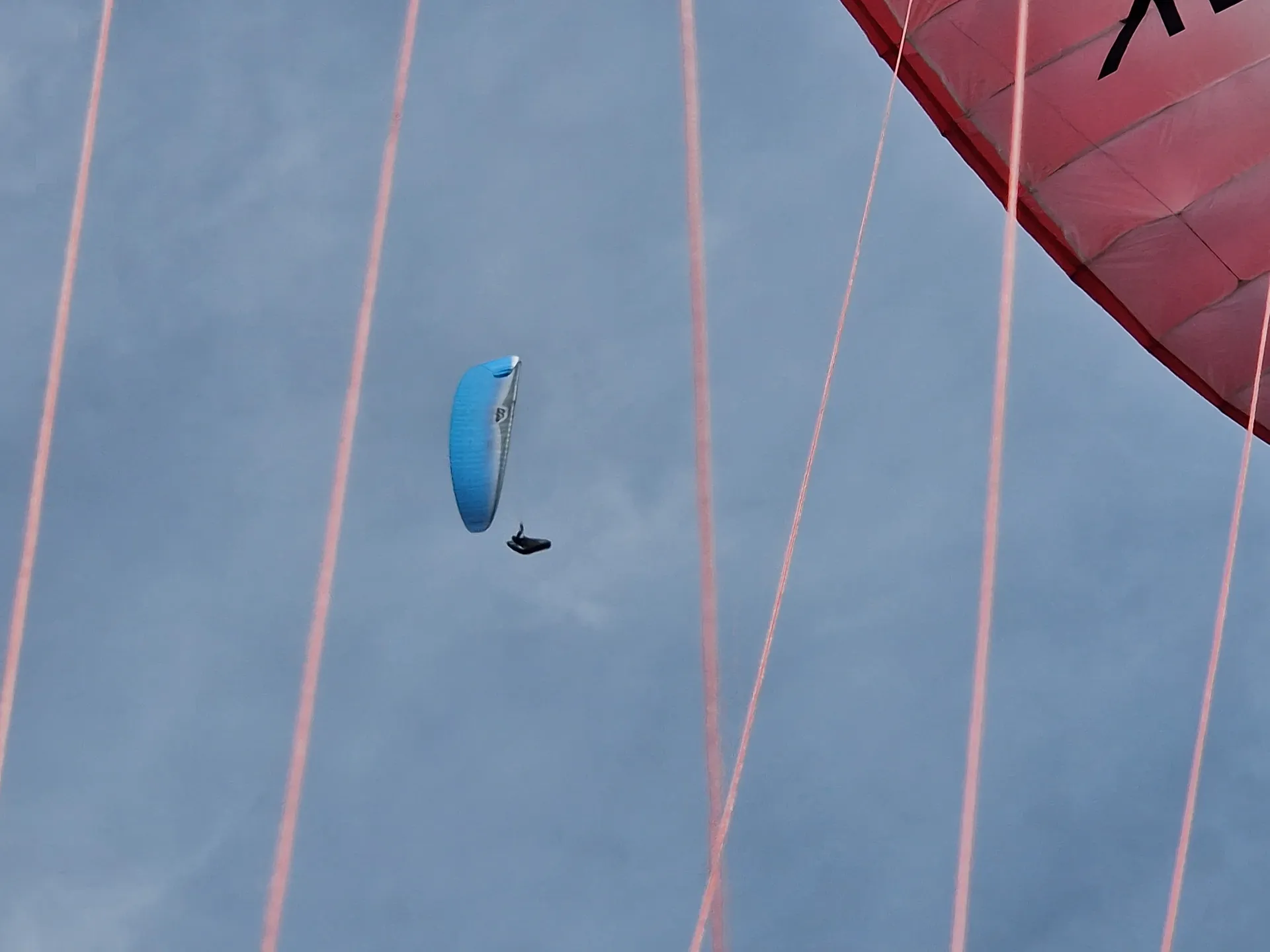 A paraglider in blue sky, seen beneath another wing